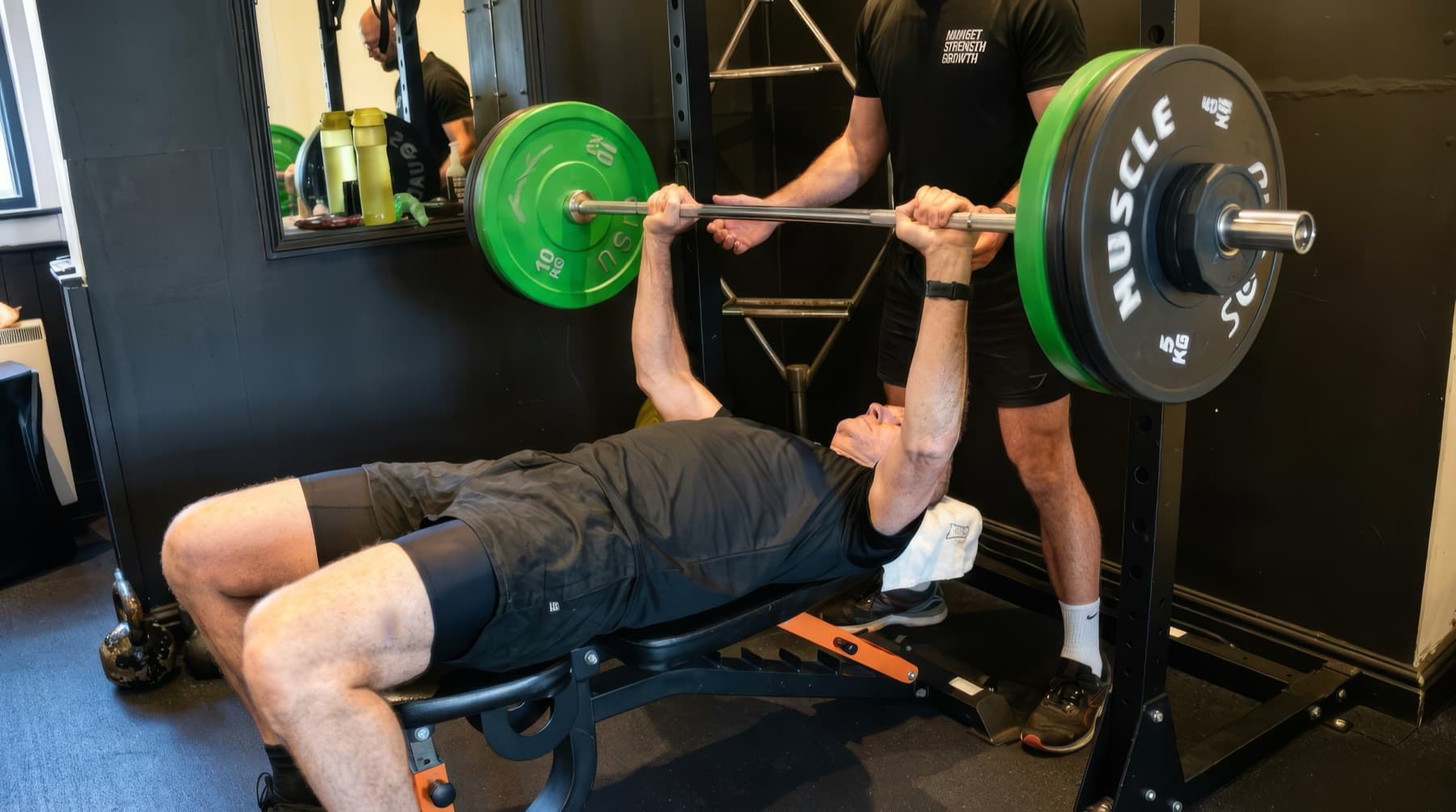 Michael Dennison spotting a client through a barbell bench press in his private studio